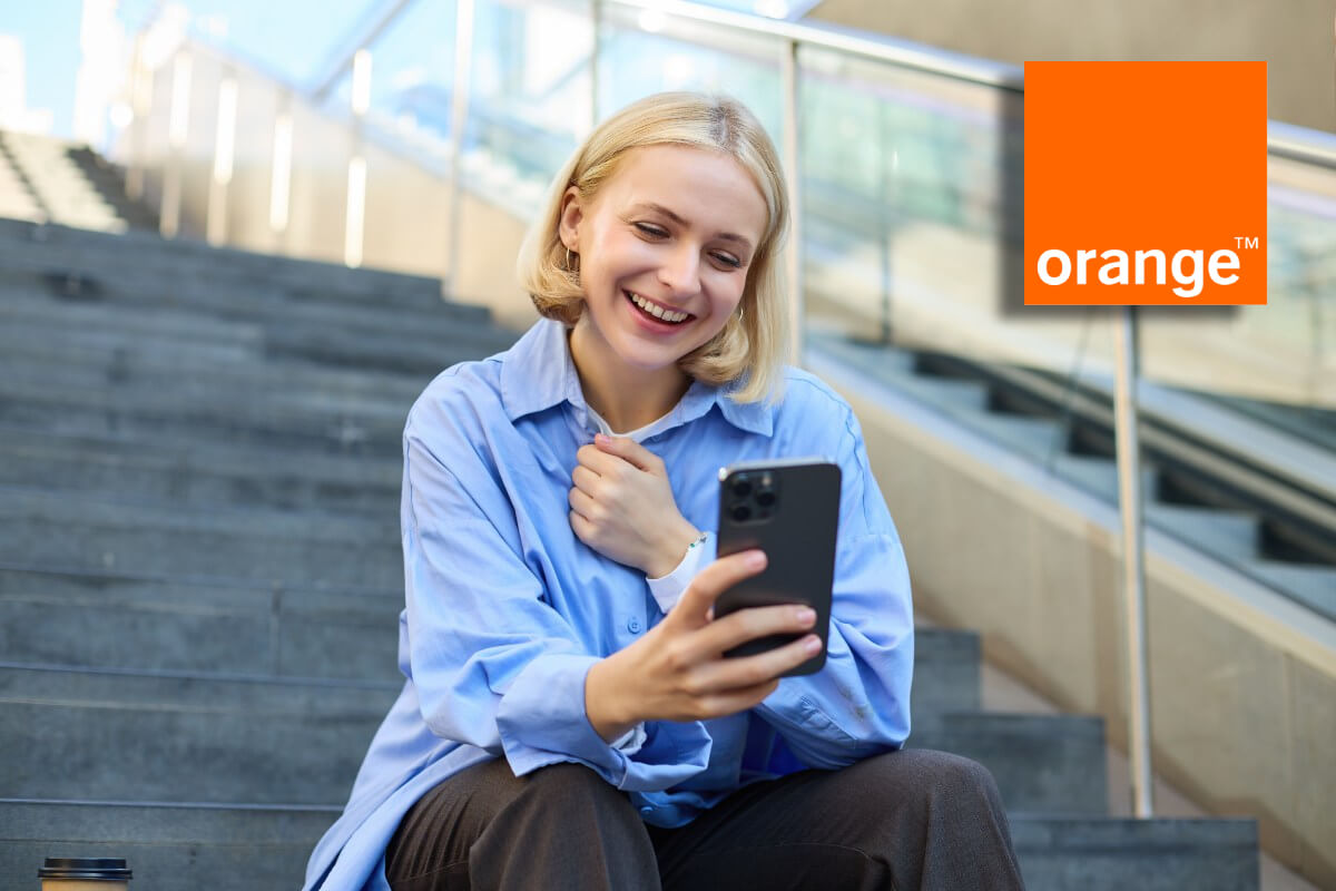 Femme assise sur marches d'escalier avec smartphone et logo d'Orange sourit, heureuse avec son forfait best-seller de 120 Go